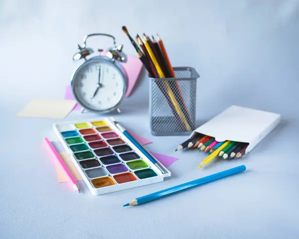 Back to school, watercolor paints, brushes and colored pencils, palette, school supplies on a gray background