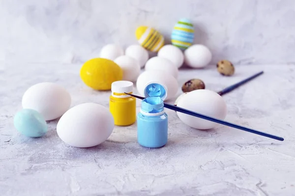 Easter eggs painted in pastel colors, yellow and blue paint, brushes on a concrete table