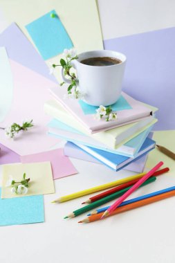 Bir fincan kahve, bir yığın kitap, kırtasiye ve kiraz çiçekleri pastel renkli kağıdın üzerinde. 