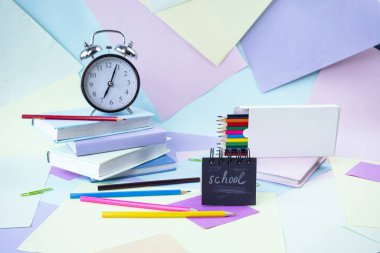 Okula, kırtasiyeye, çalar saate, kitap yığınına, kağıda ve öğrenci masasına renkli kalemlere.