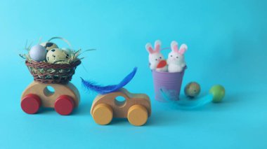 Ahşap bir oyuncak arabada Paskalya sepetinde bıldırcın yumurtası, saman ve tüy, mavi bir arka planda