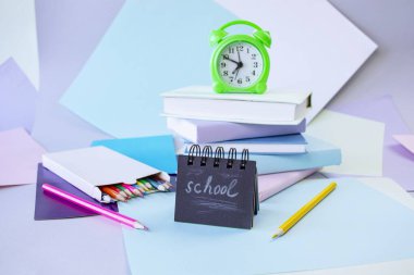 Okula, kırtasiyeye, çalar saate, kitap yığınına, kağıda ve öğrenci masasına renkli kalemlere.