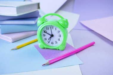 Okula, kırtasiyeye, çalar saate, kitap yığınına, kağıda ve öğrenci masasına renkli kalemlere.