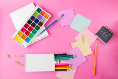 Renkli kalemler, çıkartmalar, çalar saat ve pembe arka plandaki not defteri ile okul konseptine geri dönelim.