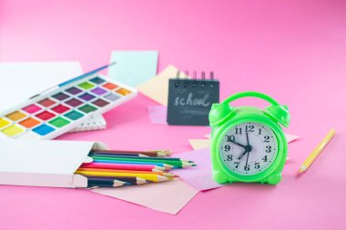 Renkli kalemler, çıkartmalar, çalar saat ve pembe arka plandaki not defteri ile okul konseptine geri dönelim.