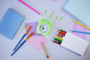 Okul konseptine geri dönersek, öğrenci masasında kağıtlar, renkli kalemler, açık arkaplanda boyalar ve rulo kağıtlar, pastel renkler var.