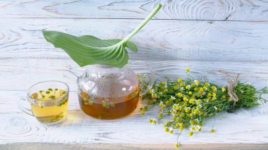 Cam çaydanlıkta papatya çiçekleri olan şifalı bitkisel çay, bir buket taze çiçek, ahşap ışıklı arka planda..