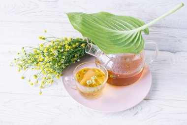 Cam çaydanlıkta papatya çiçekleri olan şifalı bitkisel çay, bir buket taze çiçek, ahşap ışıklı arka planda..