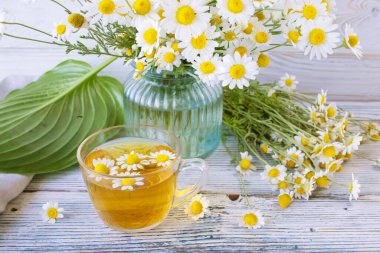 Cam bir fincanda papatya çiçekleri olan şifalı bitkisel çay, bir buket taze çiçek, ahşap bir arka planda..