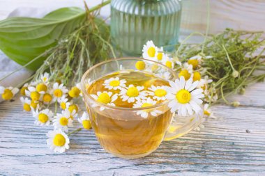 Cam bir fincanda papatya çiçekleri olan şifalı bitkisel çay, bir buket taze çiçek, ahşap bir arka planda..