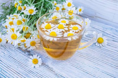 Herbal medicinal tea with chamomile flowers in a glass cup, a bouquet of fresh flowers, on a wooden light background. clipart