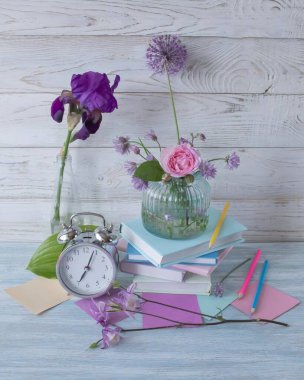 Bir yığın kitap, bir çalar saat, bir buket çiçek ve ahşap arka planda kırtasiye malzemeleri. Okula geri dön..