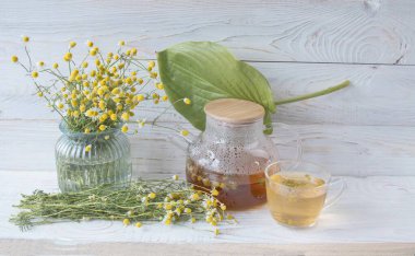 Cam çaydanlıkta papatya çiçekleri olan şifalı bitkisel çay, bir buket taze çiçek, ahşap ışıklı arka planda..