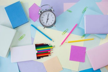 Okul konseptine geri dönelim. Alarm saati, defterler, kalemler, ataçlar ve renkli arkaplan üzerine ders kitapları, pastel renkler.