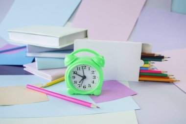 Kitap yığını, çalar saat, okul malzemeleri ve pastel renklerde yaratıcı öğrenme malzemeleri..