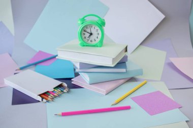 Kitap yığını, çalar saat, okul malzemeleri ve pastel renklerde yaratıcı öğrenme malzemeleri..