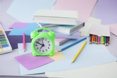 Kitap yığını, çalar saat, okul malzemeleri ve pastel renklerde yaratıcı öğrenme malzemeleri..