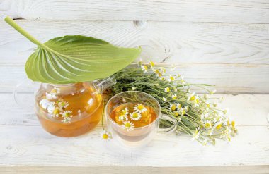 Cam çaydanlıkta papatya çiçekleri olan şifalı bitkisel çay, bir buket taze çiçek, ahşap ışıklı arka planda..