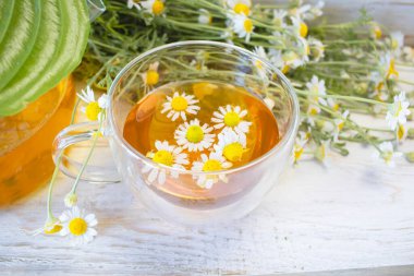 Cam çaydanlıkta papatya çiçekleri olan şifalı bitkisel çay, bir buket taze çiçek, ahşap ışıklı arka planda..