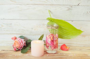 Pembe gül çiçekleri, mum ve gül yapraklı su ile kaplıca hayatı, ahşap arka planda. Alternatif tıp, aromaterapi, vücut bakımı..