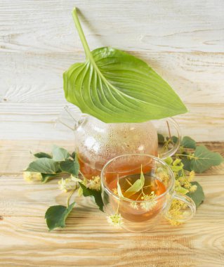 Cam bardakta ıhlamur çayı, taze ıhlamur çiçekleri, ahşap bir arka planda. Şifalı bitki çayı..