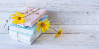 Sayfaların arasında sarı çiçekli kitap yığını, beyaz ahşap arka plan, boşluğu kopyala