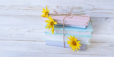 Sayfaların arasında sarı çiçekli kitap yığını, beyaz ahşap arka plan, boşluğu kopyala