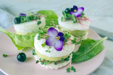 Salatalık dilimleri, mikroyeşillikler ve taze mor çiçeklerle süslenmiş beyaz peynir ile vejetaryen aperatifi..