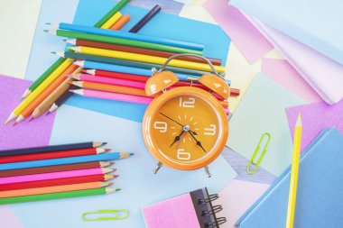 Okul konseptine geri dönelim. Alarm saati, kırtasiye ve pastel renkli kağıtlar masanın üstünde, üst görünümde, düz yerde..