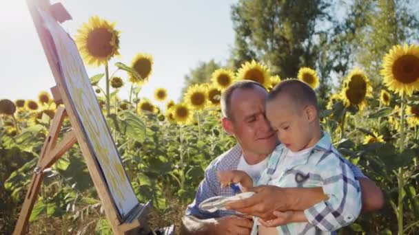 Caring Father Kisses Son Syndrome Learning Draw Canvas Sunflowers Blooming — Stockvideo