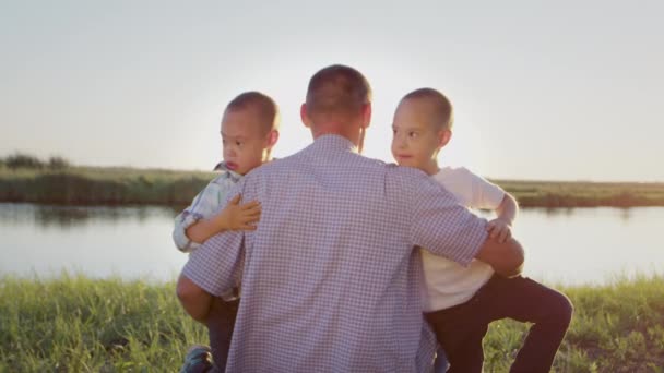 Caring Father Hugs Little Boys Siblings Syndrome Sitting Grassy River — Vídeos de Stock