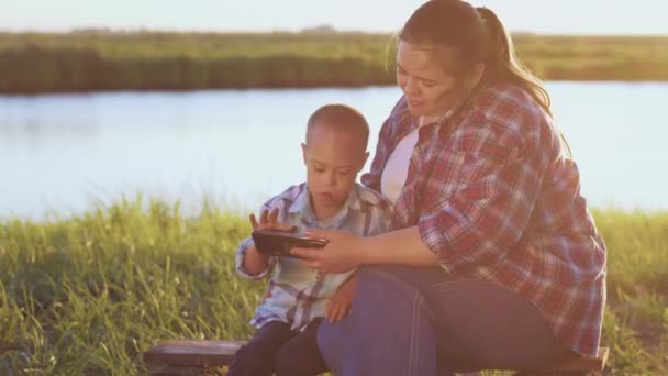 Loving Mother Lets Little Boy Syndrome Use Smartphone Sitting River — Vídeo de Stock