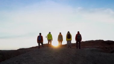 Gün batımında dağın tepesinde dikilen bir grup turistin arkası. Başarının neşesi, mutlu gezginler aktif yaşam tarzının tadını çıkarırlar.