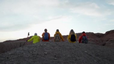 Bir grup yürüyüşçü arkadaş dağın tepesinde birlikte oturuyorlar. Başarı sevinci, seyahat yolculuğunda başarı ve gün batımında aşırı turizm.