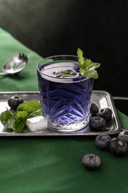 Colorful purple blueberry cocktail with fresh berries and mint. Dark, moody background