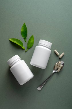 Yeşil arka planda beyaz hap şişeleri. Sağlıklı gıda takviyeleri, vitaminler ve ilaçlar.