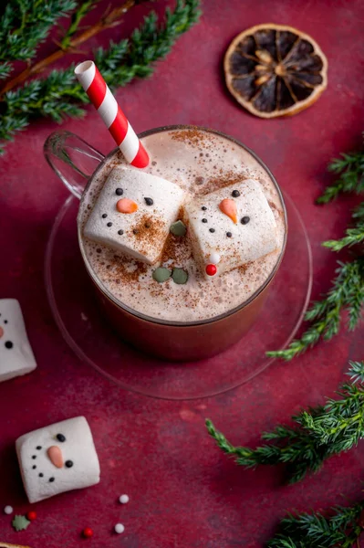 Red mug with hot chocolate and melted marshmallow snowman, red festive background.