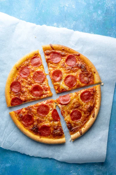 Pepperoni pizza sliced, on blue background, one pizza, top view.