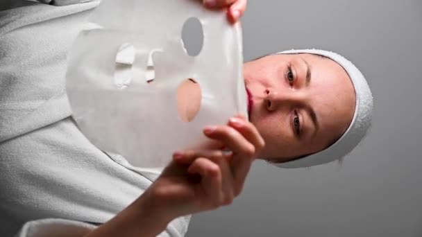 テキスタイルフェイスマスクを適用する女性 スキンケア 化粧品の手順 垂直ビデオ 高品質のフルHd映像 — ストック動画