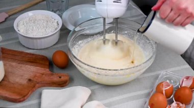 Adding oil and mixing eggs with sugar. Female hands using hand mixer, cooking sweet dessert. 