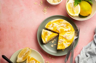 Lemon cheesecake tart or pie, with fresh lemons. Pink background.