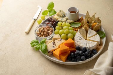 Cheese board, platter with assorted various cheeses, fruits, nuts and snacks. Warm background