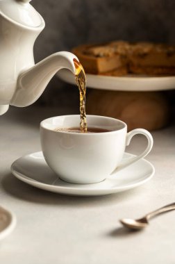 Sıcak çayı beyaz, seramik bardakta, kekle servis edilir.