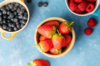 Fresh berries. Blueberry, raspberry and strawberry in colourful bowls. Blue background, top view