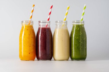 Bottles with fruit smoothies and colourful straws. Healthy detox drinks, bright background.