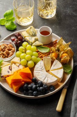 Cheese plate with various cheeses, fruits, nuts and snacks. Dark background