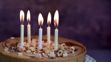 Burning candles on birthday cake, dark background.