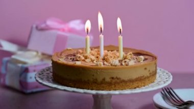 Three burning candles on birthday cheesecake pink background. High quality 4k footage