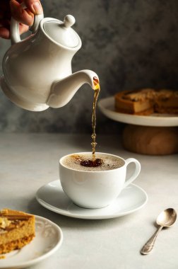 Pouring hot black tea in white, ceramic cup, served with cake