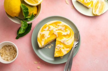 Lemon cheesecake tart or pie, with fresh lemons. Pink background.
